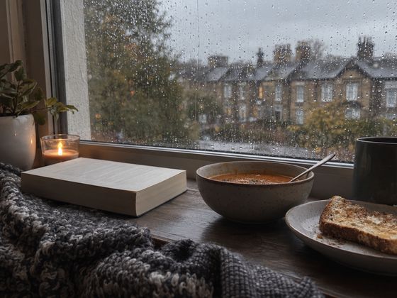 Soup, toast and a finished book on a windowsill on a rainy day